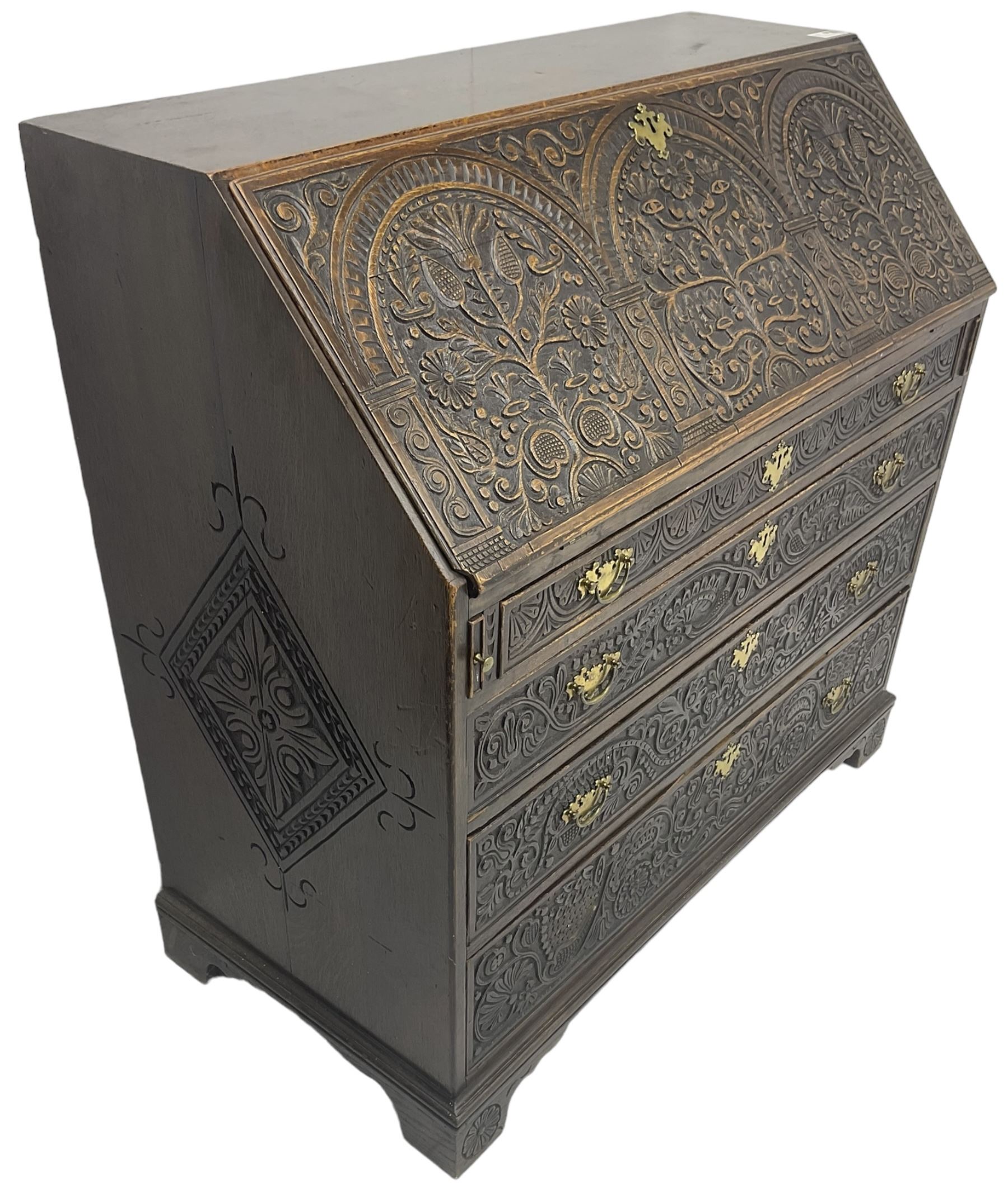 18th century heavily carved oak bureau, the fall front relief carved with three arches enclosing plants and flower head decoration, the interior fitted with pigeonholes, drawers and cupboard, four graduating cock-beaded drawers below, carved with lunettes and trailing foliage decoration, on bracket feet