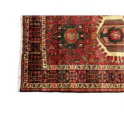 Persian Karajeh red ground runner, the field set with seven trailing geometric medallions, the field decorated all over with stylised plant motifs, the multiple banded border with repeating geometric flower head patterns