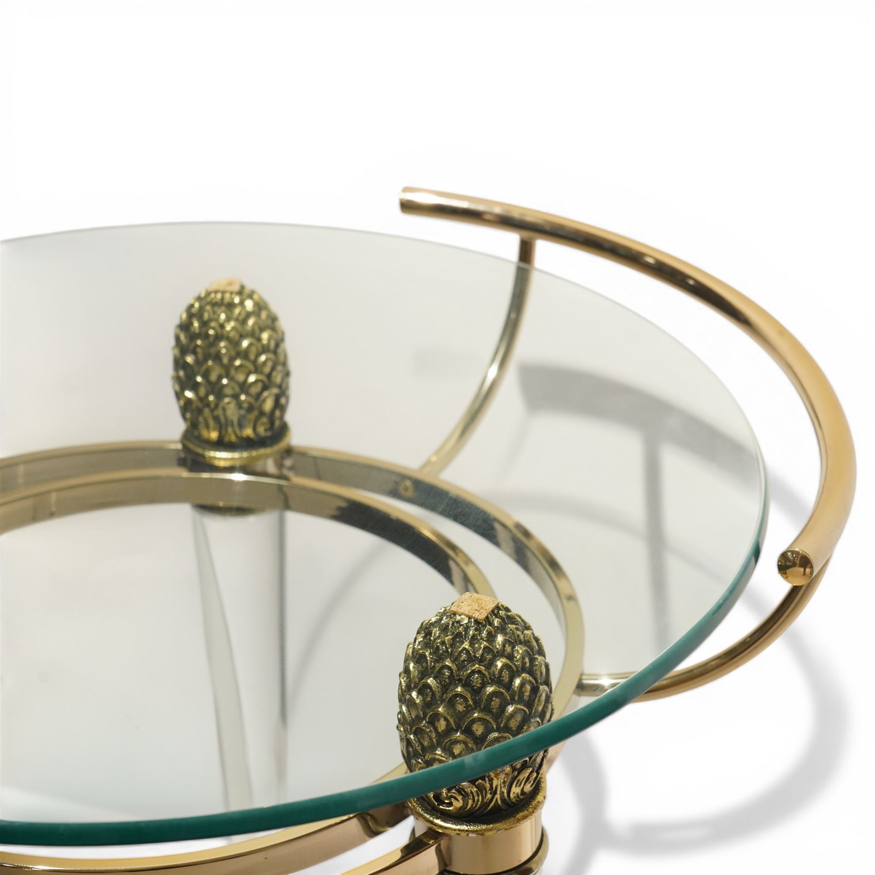 Hollywood Regency style gilt metal and glass serving trolley, circular top in a polished brass surround with three pineapple finials, supported on clear column legs, lower glass shelf enclosed by a brass gallery, terminating in castors