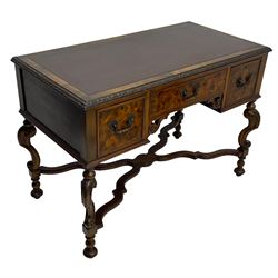 20th century figured walnut writing table, rectangular top with inset leather writing surface and foliate carved edge, fitted with three drawers over kneehole with S-scroll carved brackets, on acanthus carved S-scroll supports terminating to turned feet, united by a shaped and stepped X-framed stretcher rails with moulding 