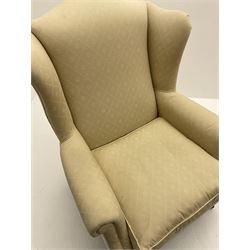 Late 20th century traditional shaped wingback armchair upholstered in pale fabric, turned and fluted front supports with brass cups and castors