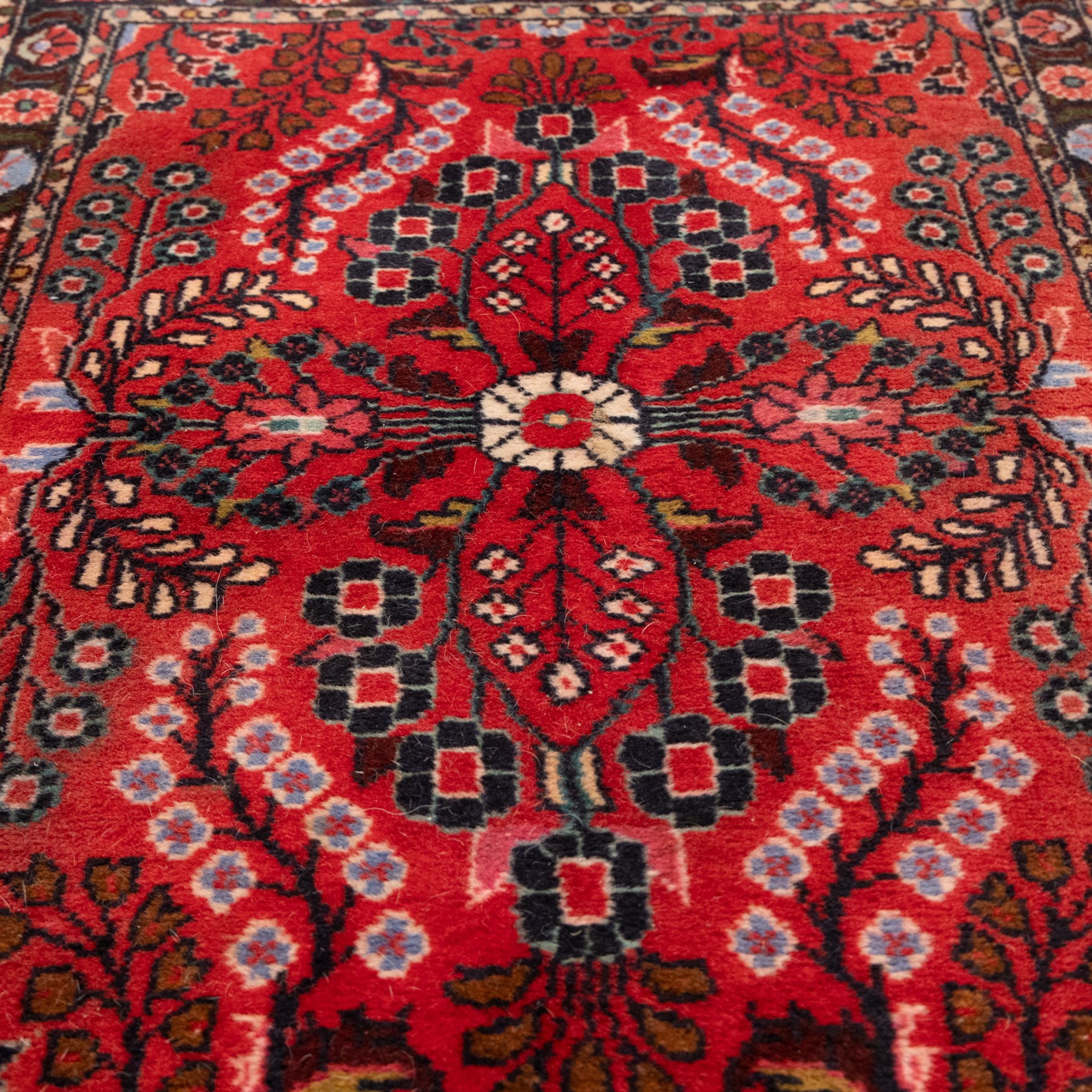Two Persian rugs, the larger with a crimson field decorated with three linked indigo medallions amongst flowering tendrils, shaped floral spandrels and an indigo palmette border, (161cm x 129cm), the smaller with a crimson field centred by an ivory rosette amongst stylised flowering plants, within a dark floral border, (114cm x 79cm) (2)