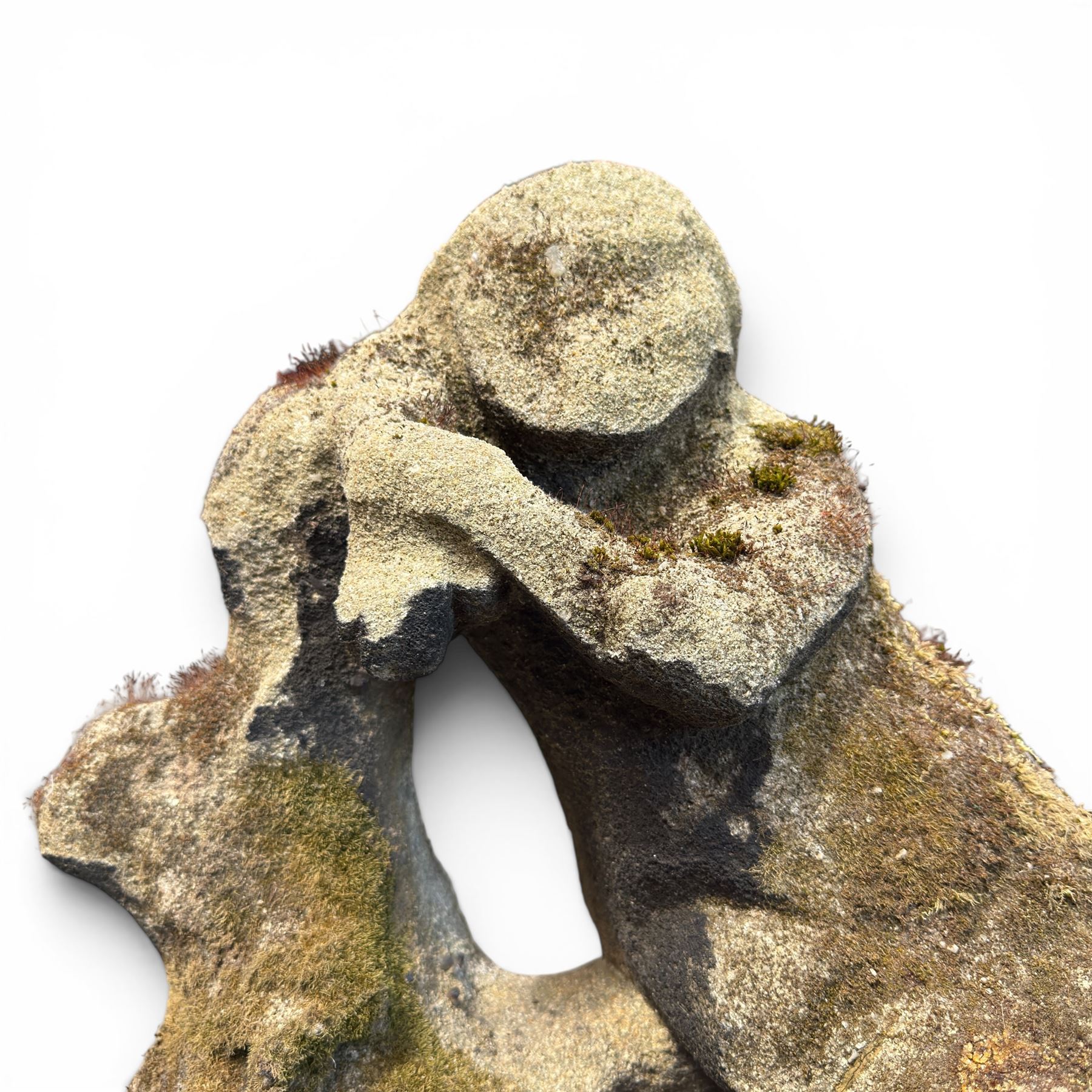 Carved composite stone garden figure, depicting a seated child with folded arms, weathered finish with moss and lichen growth, raised on an integral naturalistic base