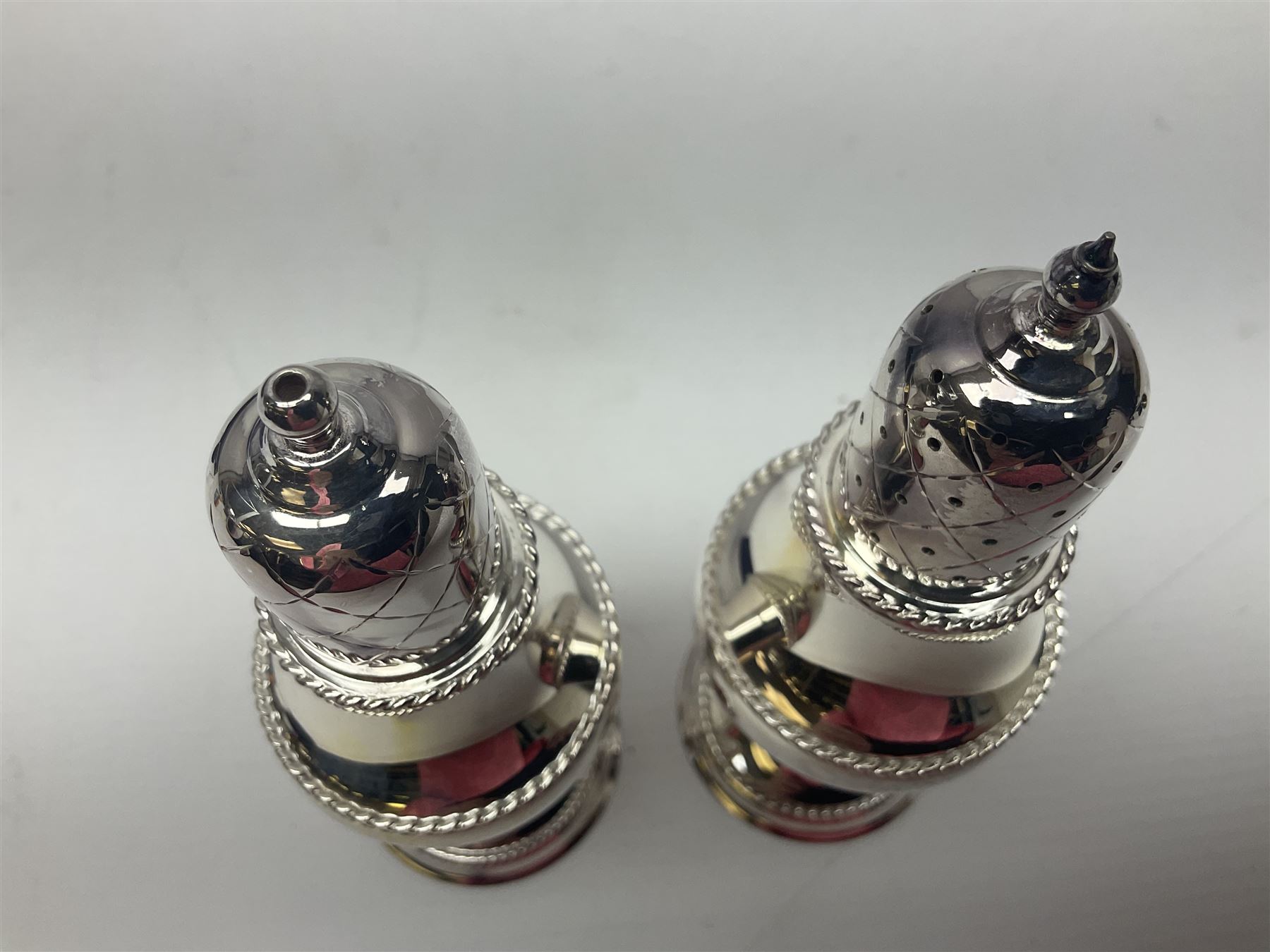 Silver plated two piece cruet set, comprising salt shaker and pepper shaker, both of waisted form with engraved rope twist borders, the removable pierced covers each with engraved lattice decoration, upon a circular spreading foot, H13.3cm, contained within velvet lined fitted case