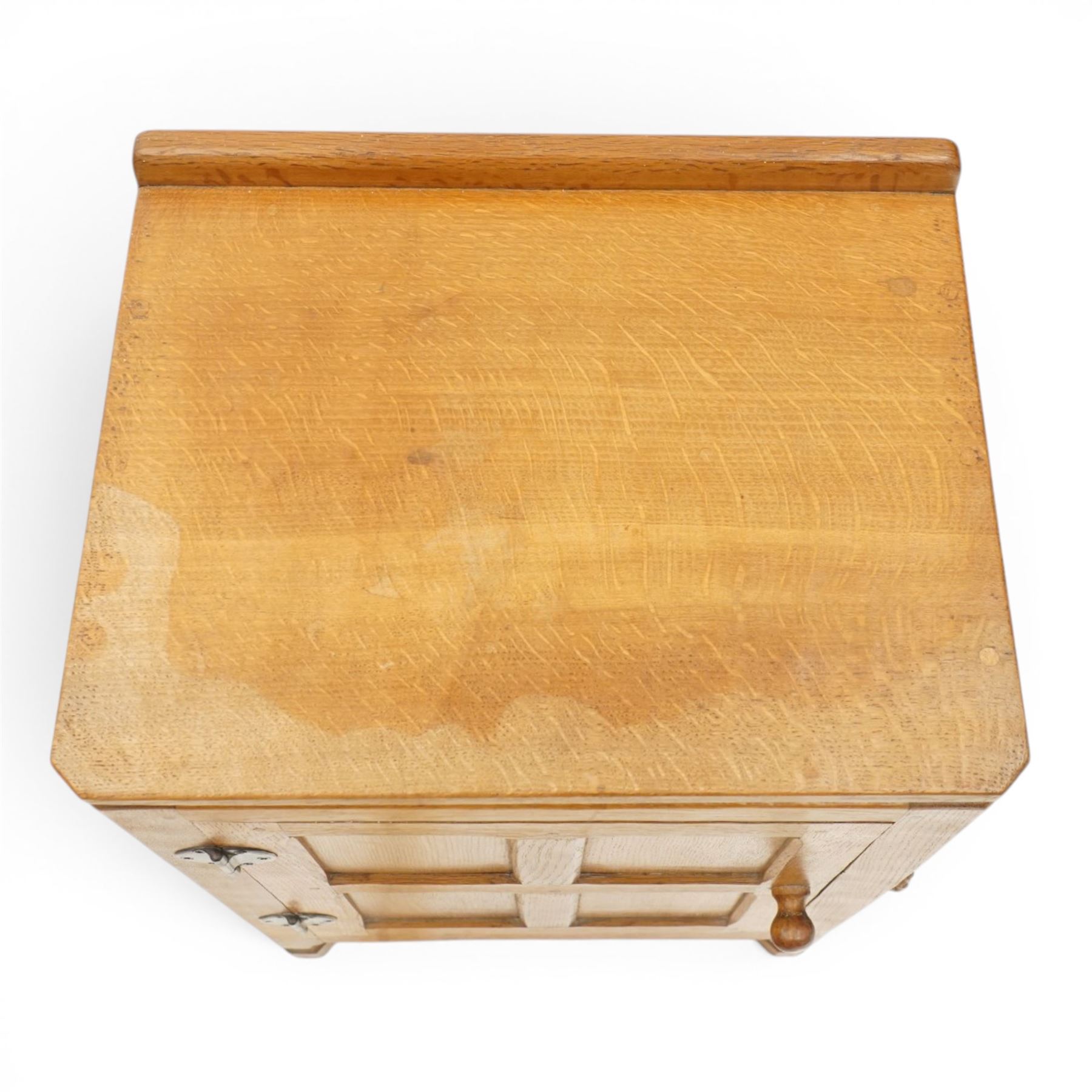 Mouseman - adzed and panelled oak bedside cupboard of small proportions, raised back over rectangular canted top, fitted with single panelled cupboard door with chamfered rails and turned knob handle, enclosing single shelf, raised on octagonal feet,  carved with mouse signature, by the workshop of Robert Thompson of Kilburn