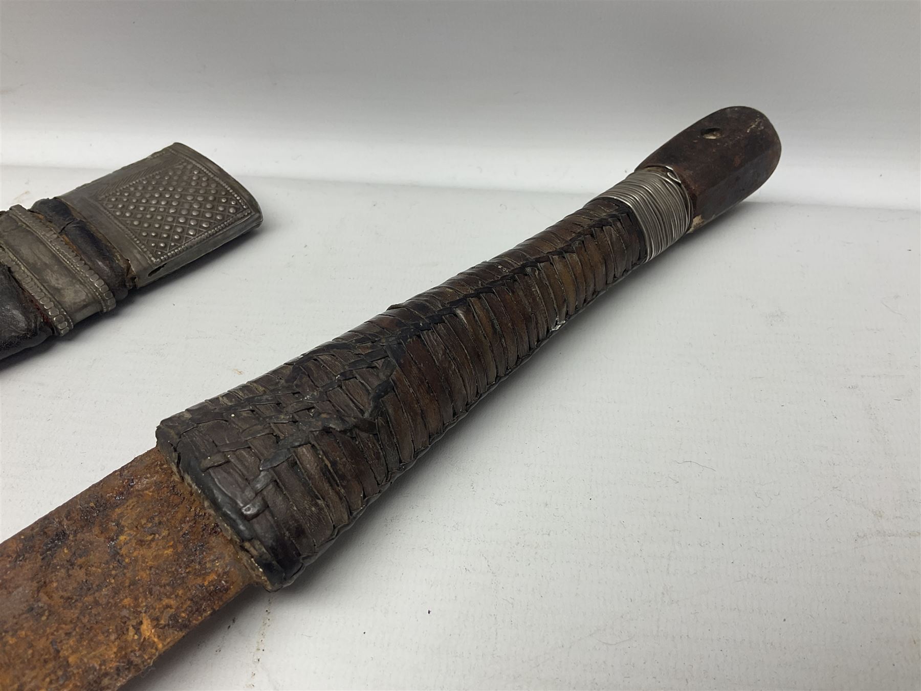 Omani presentation sword kattara, with 77cm  broad slightly curved single edge blade with two fullers, leather bound hilt woven with silver wire decoration and iron pommel;  in tooled leather scabbard with chased silver mounts and presentation plaque 'To Capt. D.M. Naylor From C Company NFR Oman Dec 1962' (Northern Frontier Regiment) L99cm overall