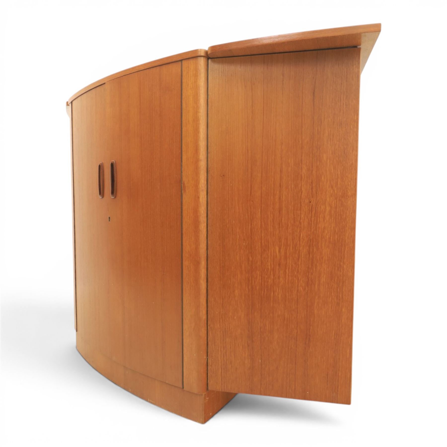 Turnidge of London - Mid 20th century teak drinks cabinet, shaped top with hinged fold-out side sections, twin doors with recessed handles enclosing fitted shelving and serving surfaces, sliding glass doors to the back, on a plinth base above castors