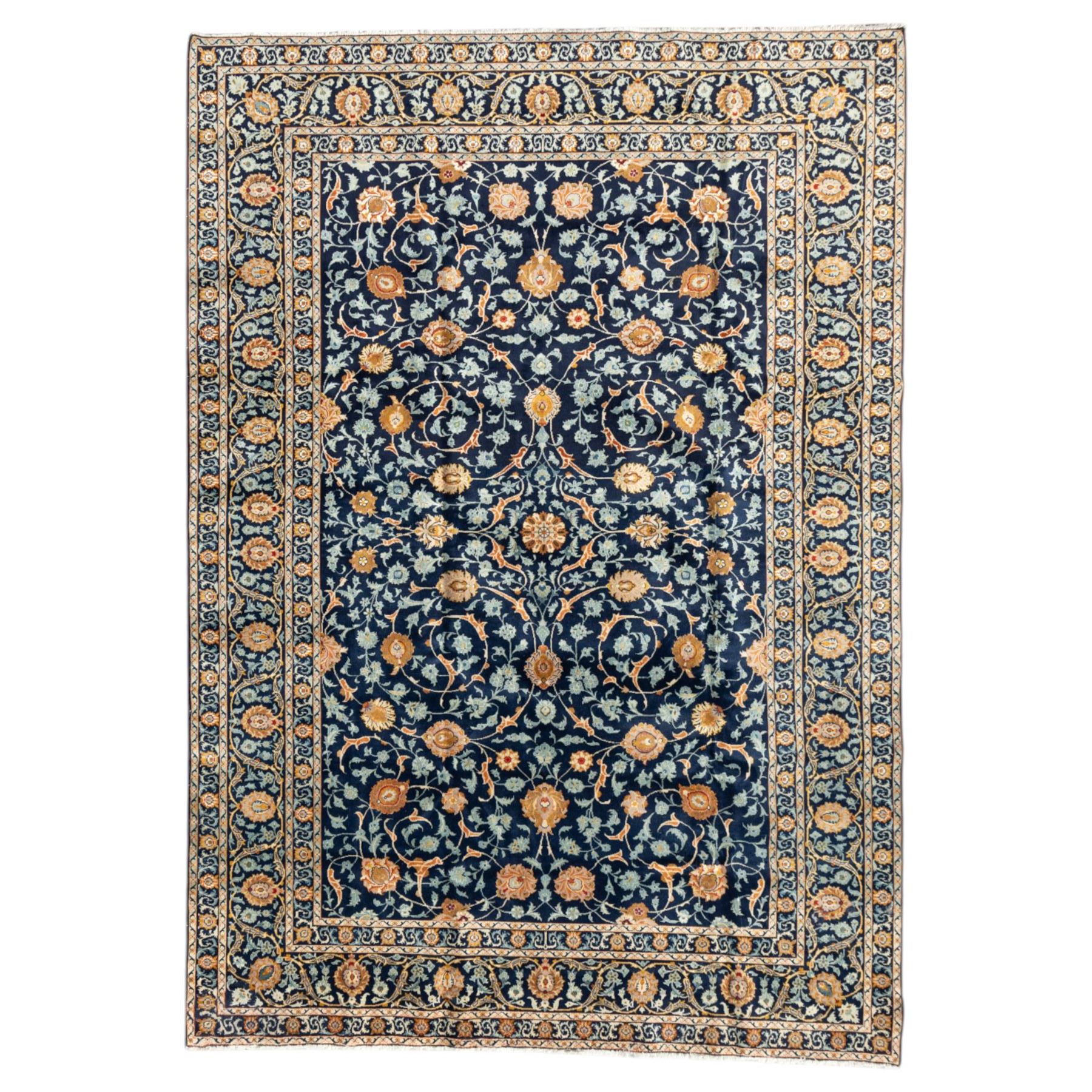 Persian Kashan carpet, navy field with an all-over design of scrolling vines, palmettes and rosettes in gold and pale blue, enclosed by multiple floral borders with stylised palmette motifs, originating from Central Iran