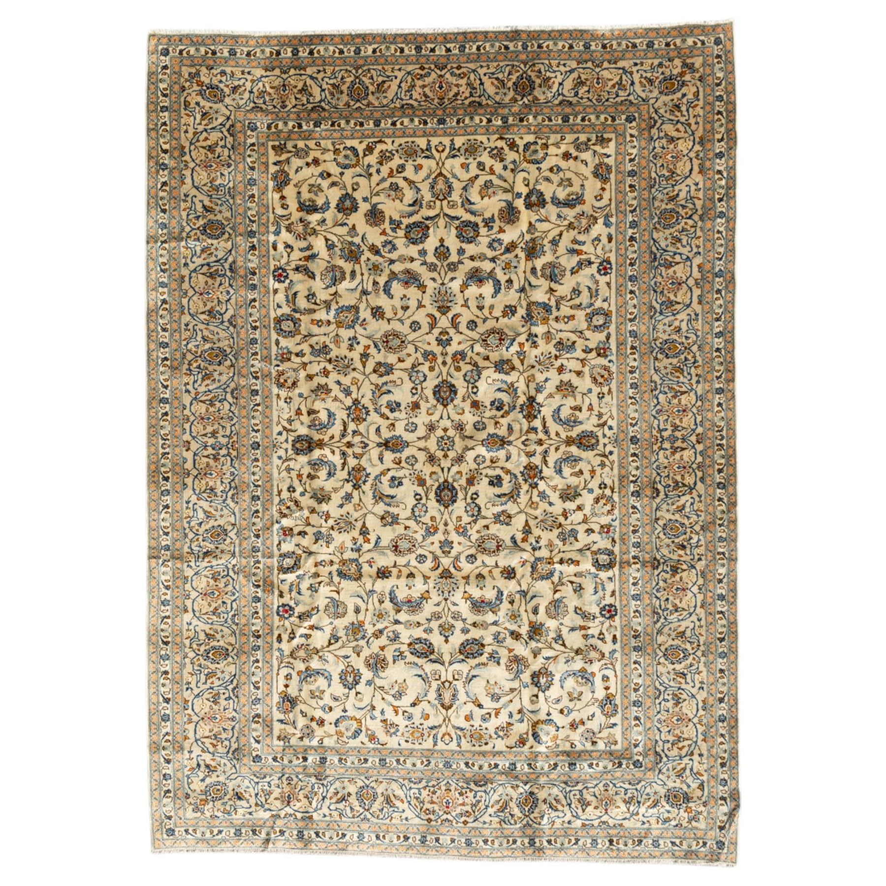 Central Persian Kashan rug, cream ground densely decorated with interconnected floral stems, rosettes and palmettes in shades of blue and gold, framed by layered foliate borders, woven in the Kashan region of Iran