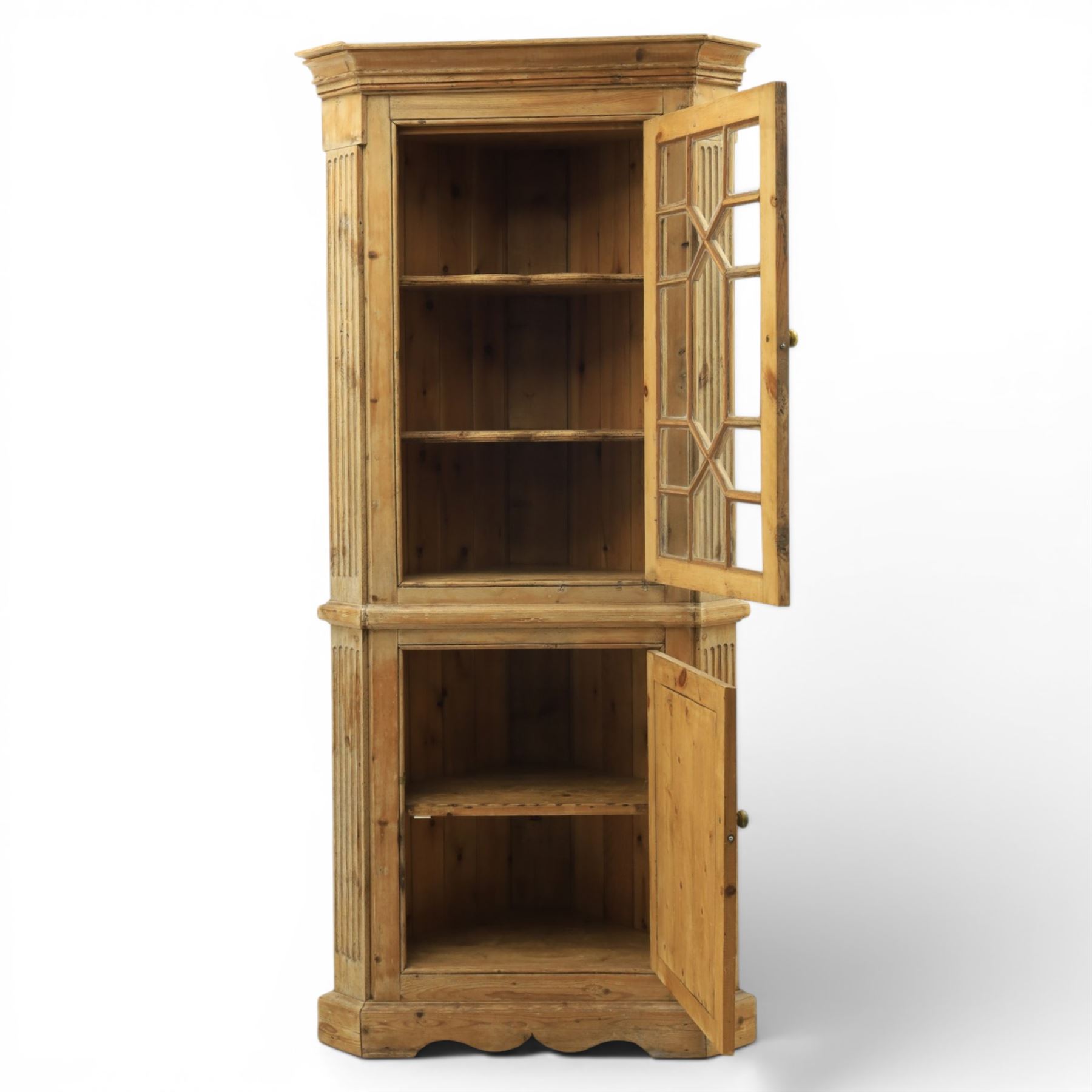 19th century stripped pine corner cabinet, projecting cornice flanked by fluted sides, astragal glazed upper door with brass knob, lower section with fielded panelled door, raised on a shaped plinth base 