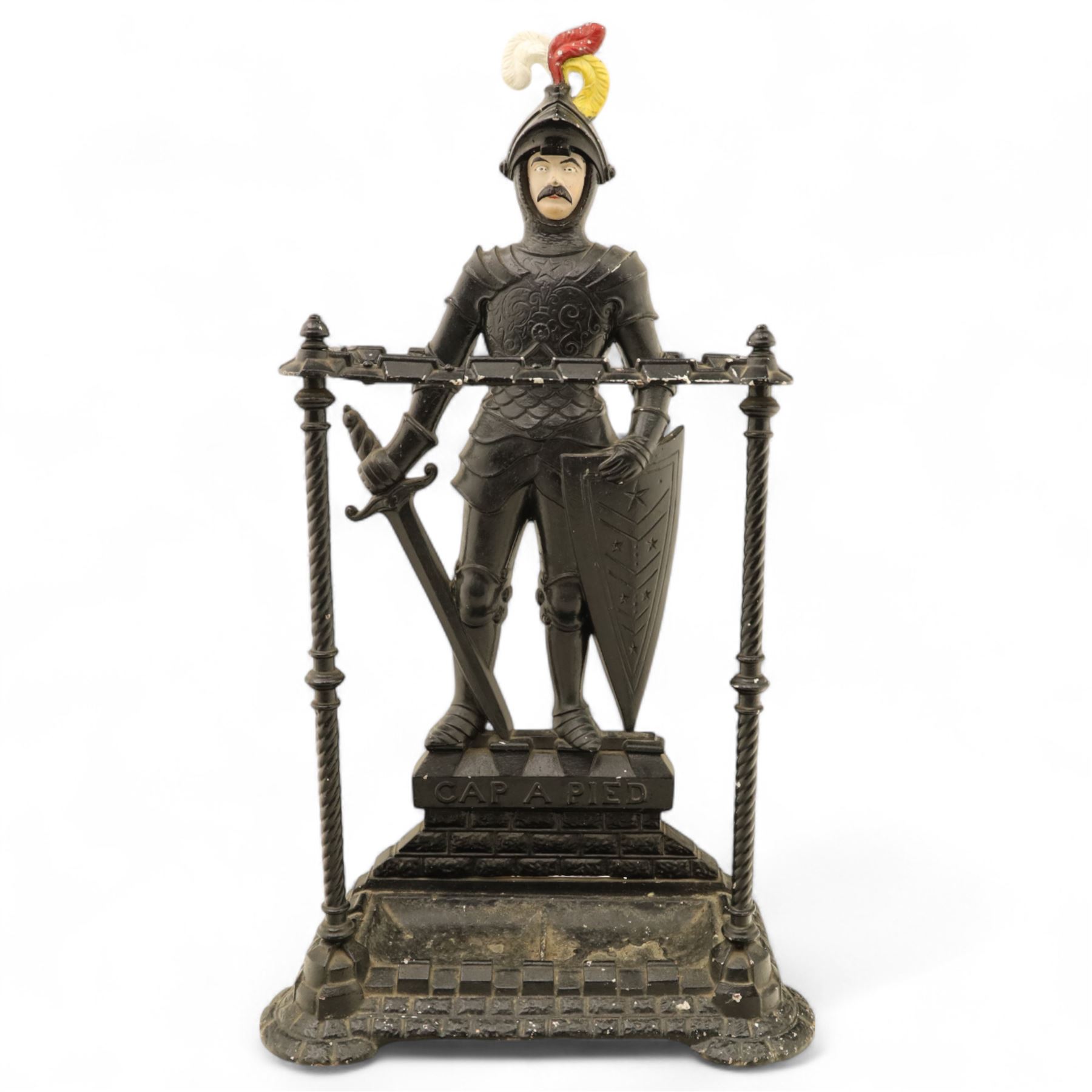 Early 20th century painted cast iron hall stand, formed as a standing armoured figure with red and yellow feathered crest, twin rails and integral drip tray with castellated edge