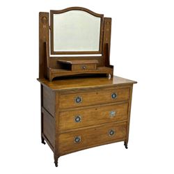 Early 20th century Arts and Crafts oak dressing chest, the arched mirror flanked by floral marquetry inlaid uprights above a shelf and drawer, over three long drawers with square hammered metal plates and circular pulls, on slender supports with castors