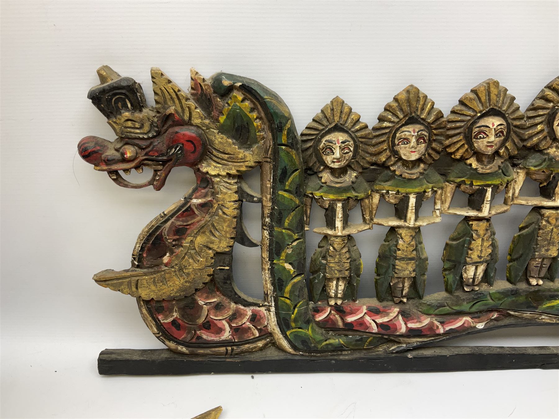 Balinese wood wall panel carved as a dragon boat with passengers, painted in reds and greens with gilding, together with a carved wood figure of Ganesh Deity decorated with gilt, raised upon circular lotus flower plinth, H78cm