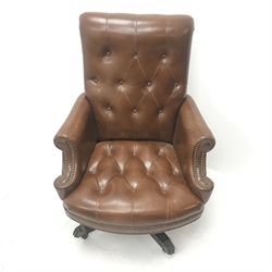 20th century captains swivel armchair, upholstered in deep buttoned studded brown leather, raised on reeded cruciform base with brass hairy paw terminals and casters,
