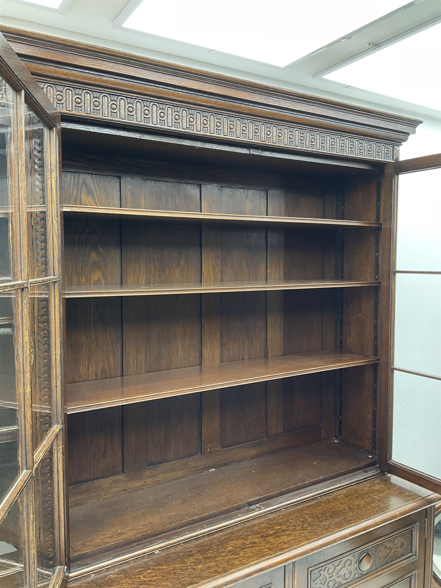 Waring and Gillow - oak bookcase on cupboard, projecting cornice over arcade frieze, guilloche upright decoration, the top section enclosed by three astragal glazed doors, the lower section enclosed by three geometric panelled doors with blind fretwork decoration, on turned feet
