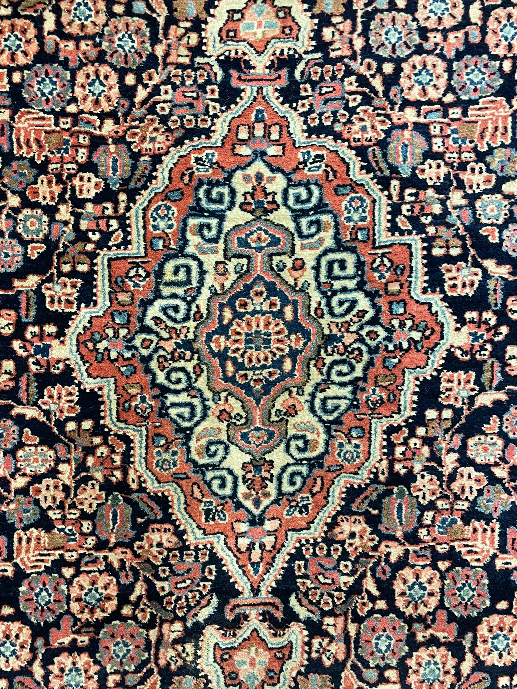 Persian indigo ground rug, the field decorated with intricate interlaced foliage branches and small flower heads, shaped floral design central medallion, the border decorated with scrolling branch and flower heads within guard bands 