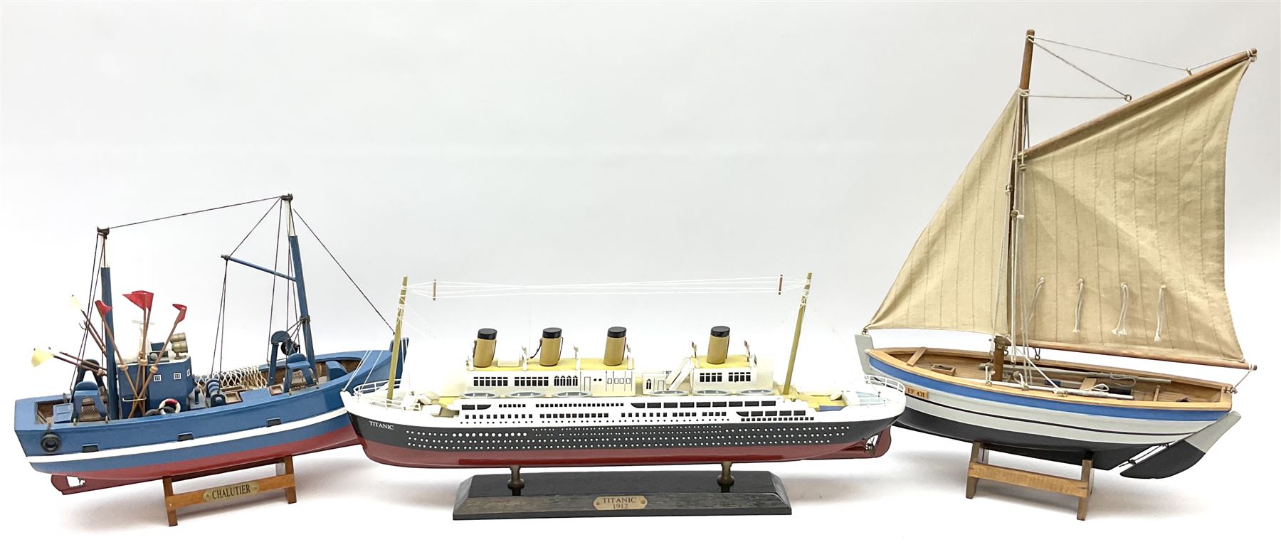 Wooden model of RMS Titanic, on a fixed black stand bearing plaque inscribed 'Titanic 1912', L54cm, H22cm, together with model of a sloop, gaff rigged on stand bearing plaque inscribed 'Sloop' L32cm, H42cm; and model of a fishing trawler on a stand bearing plaque inscribed 'Chalutier' L35cm, H28cm (3)