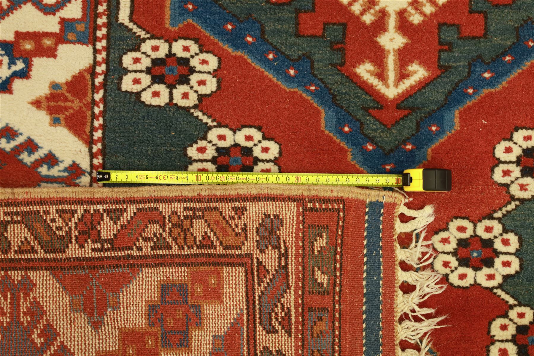 Caucasian Soumak rug, red madder field and teal panels, with bold stepped diamond medallion with hooked motifs and cruciform devices, and floral rosette clusters, surrounded by an ivory border with large hooked diamonds and stylized ram's horn devices, flanked by narrow guard stripes




