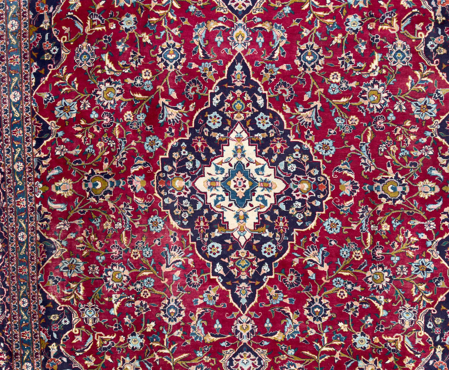 Pair of Persian wool rugs, each with rich red ground, one centred with a diamond-shaped medallion and navy spandrels within a floral field, the other with radiating floral medallion and scrolling foliate motifs, both enclosed by multiple borders with palmette and flowerhead designs, from the region of Kashan 291x376, 299 x 378 