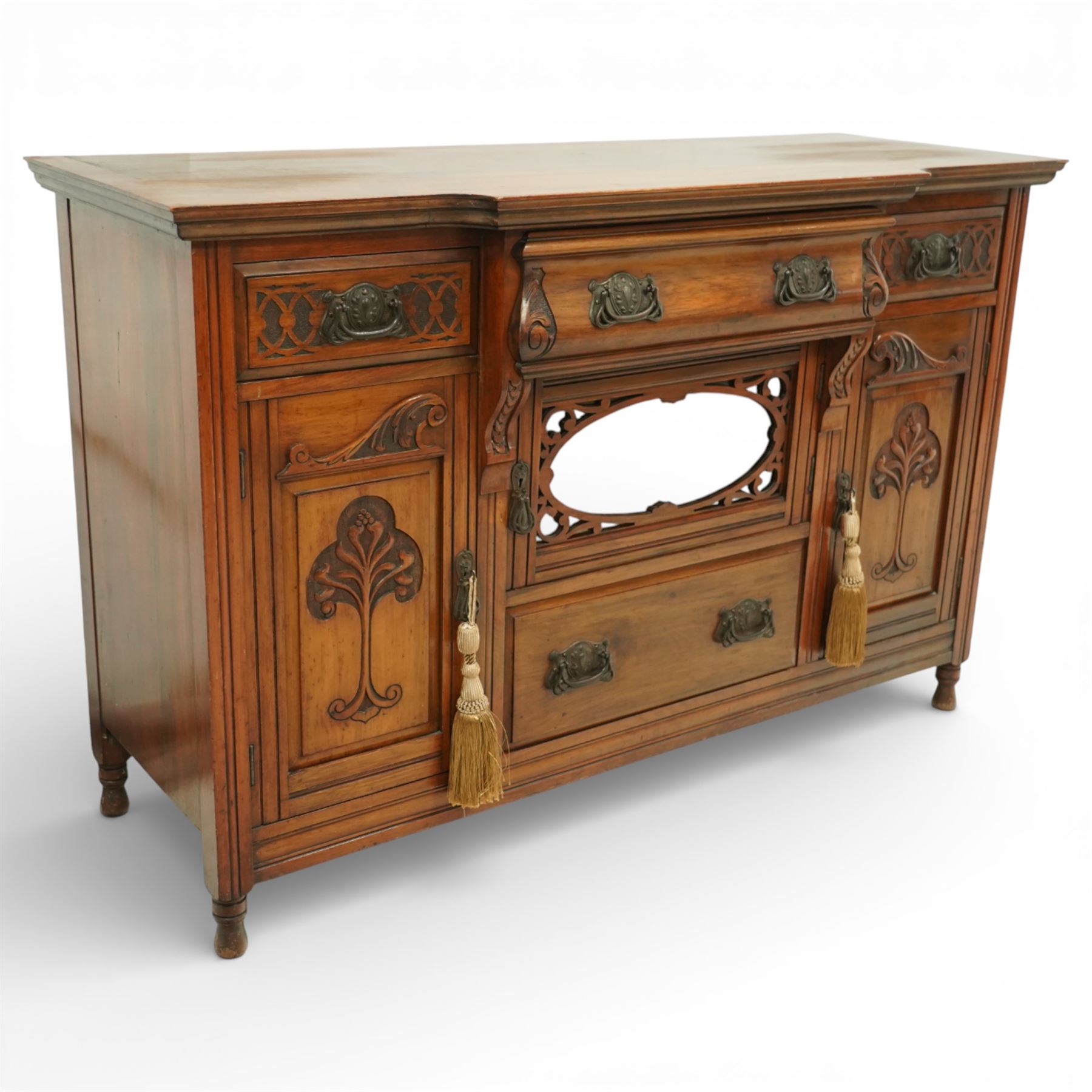 Late 20th century Art Nouveau walnut sideboard, the moulded rectangular top above a run of three drawers, the outer drawers with blind fretwork decoration and applied metal handles, the centre drawer with scroll carved terminals, below a central mirrored cupboard door with oval panel and pierced surround, flanked by carved panel doors with sinuous foliate motifs, on turned supports
