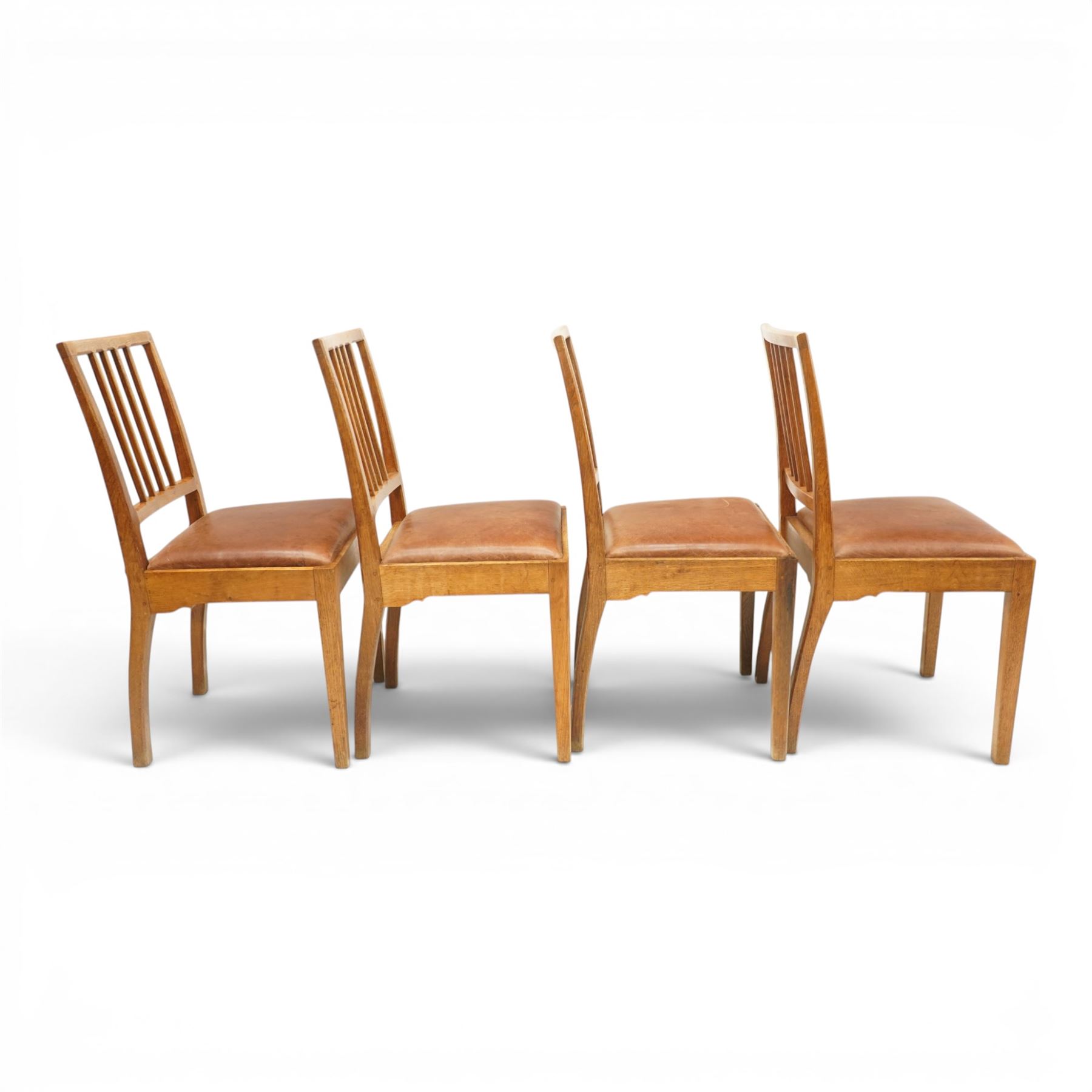 Acornman - set of four oak dining chairs, chamfered slatted back, tan leather drop in seat, raised on square supports with carved acorn signature, by the workshop of Alan Grainger of Brandsby