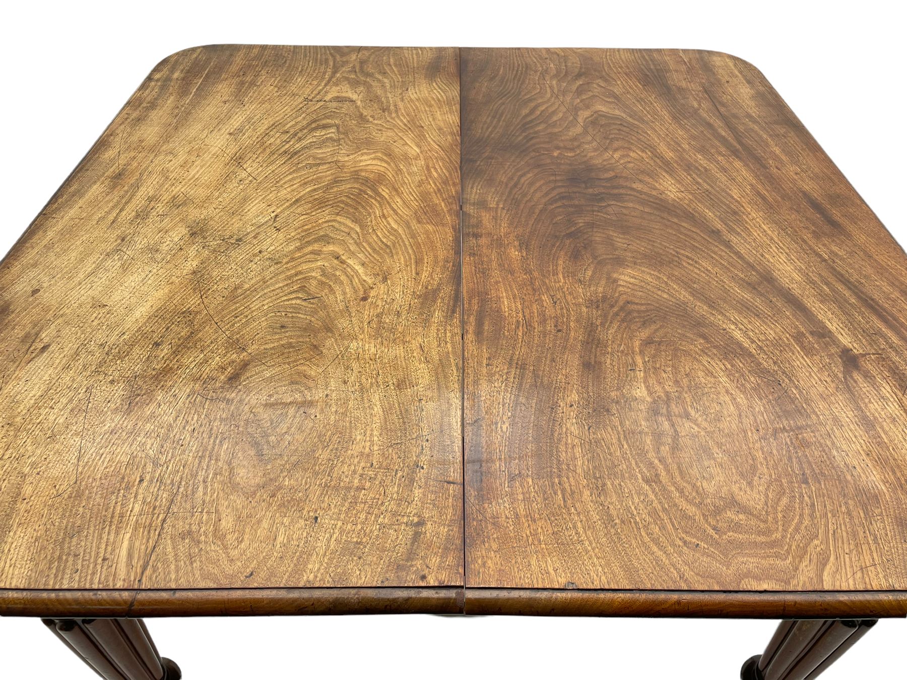 Early 19th century figured mahogany extending dining table, the rectangular top with moulded edge and rounded corners, pull-out action with three additional leaves, raised on turned and lobe carved supports with brass cup castors