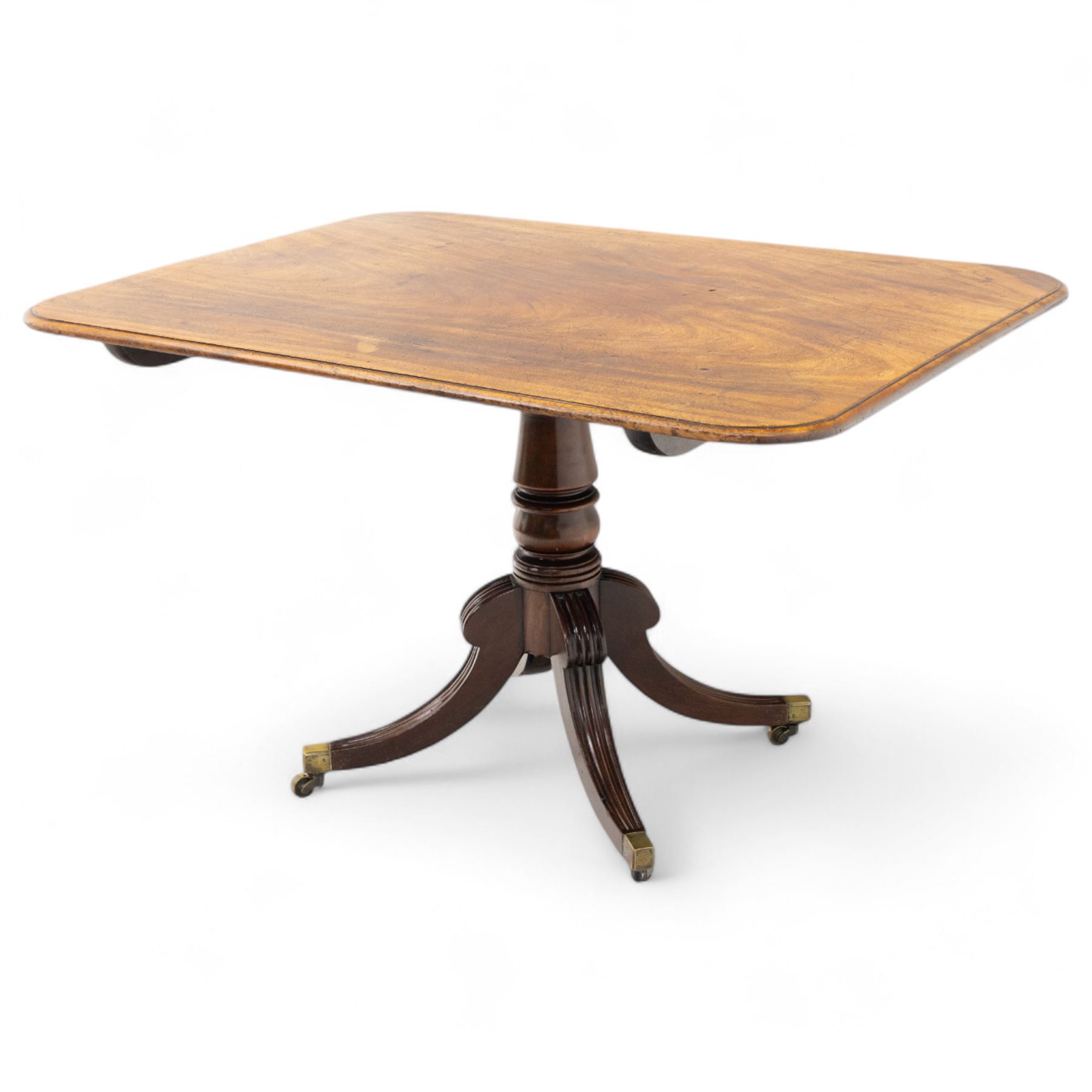 George IV mahogany breakfast table, rectangular tilt-top with reeded edge, rounded corners, supported on a turned column and raised on a quadripartite base with reeded down-swept legs terminating in brass cap castors