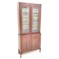 19th century mahogany bookcase on cupboard, two glazed doors with later applied advertising writing for ‘S. Gillespie Haberdashery’, the cupboard enclosed by two arched figured panelled doors, cabriole feet