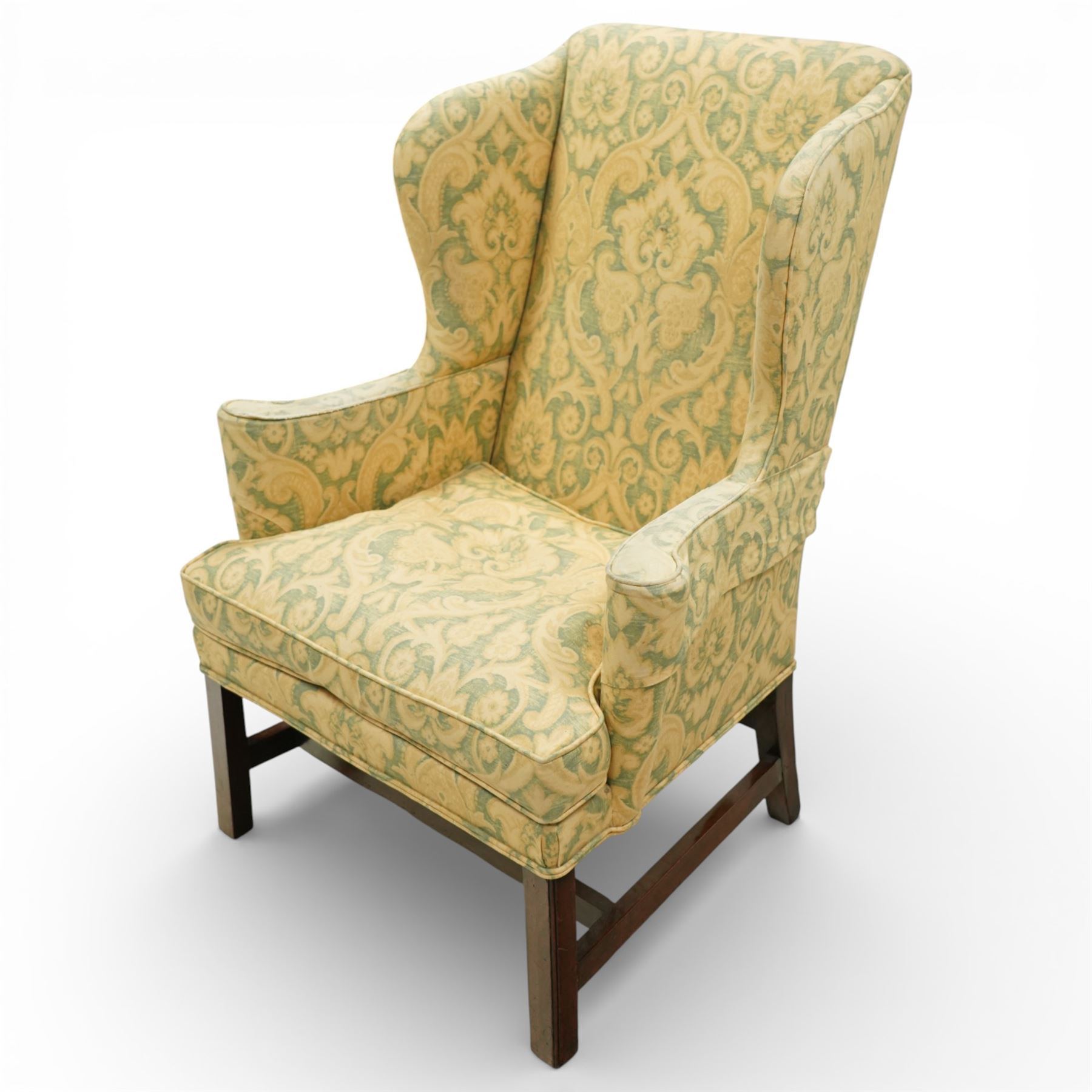 George III wing back armchair, the tall upholstered back with deep wings and gently shaped outline, padded arms flowing into the seat, loose cushion seat upholstered in a foliate patterned fabric, standing on square legs joined by stretchers