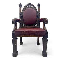 Late Victorian Gothic-revival armchair, arched crest rail carved with tracery and trefoil detail, padded circular back and seat, brass studded burgundy leather upholstery, shaped armrests with scrolled terminals, on square tapering supports