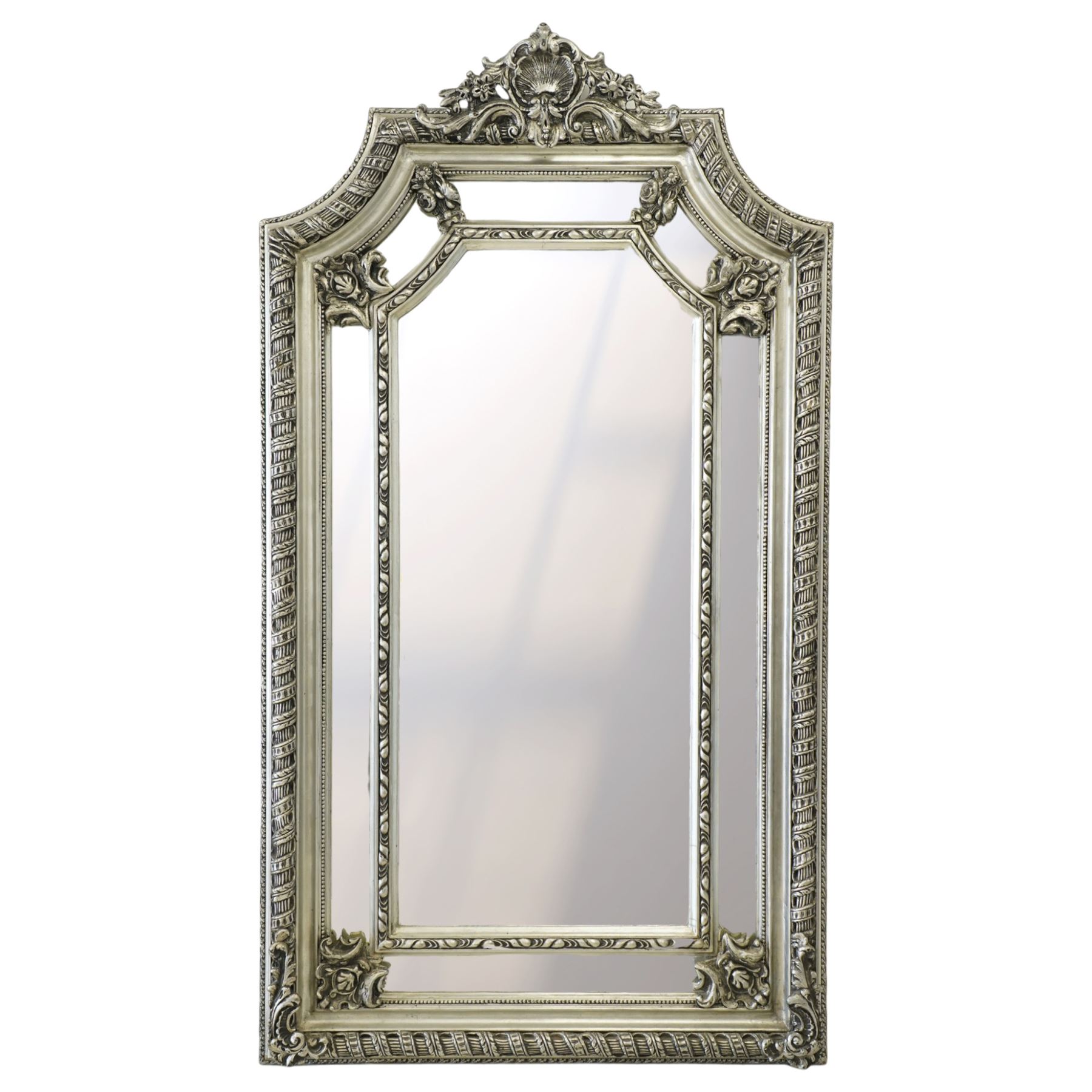 Impressive Baroque Revival mirror in antique silvered finish, the pierced cartouche shell pediment flanked  by C-scrolls and flower heads, the outer frame with ribbon-twist motifs throughout, the central arched bevelled plate surrounded by further rectangular mirror panels with cartouche mounts