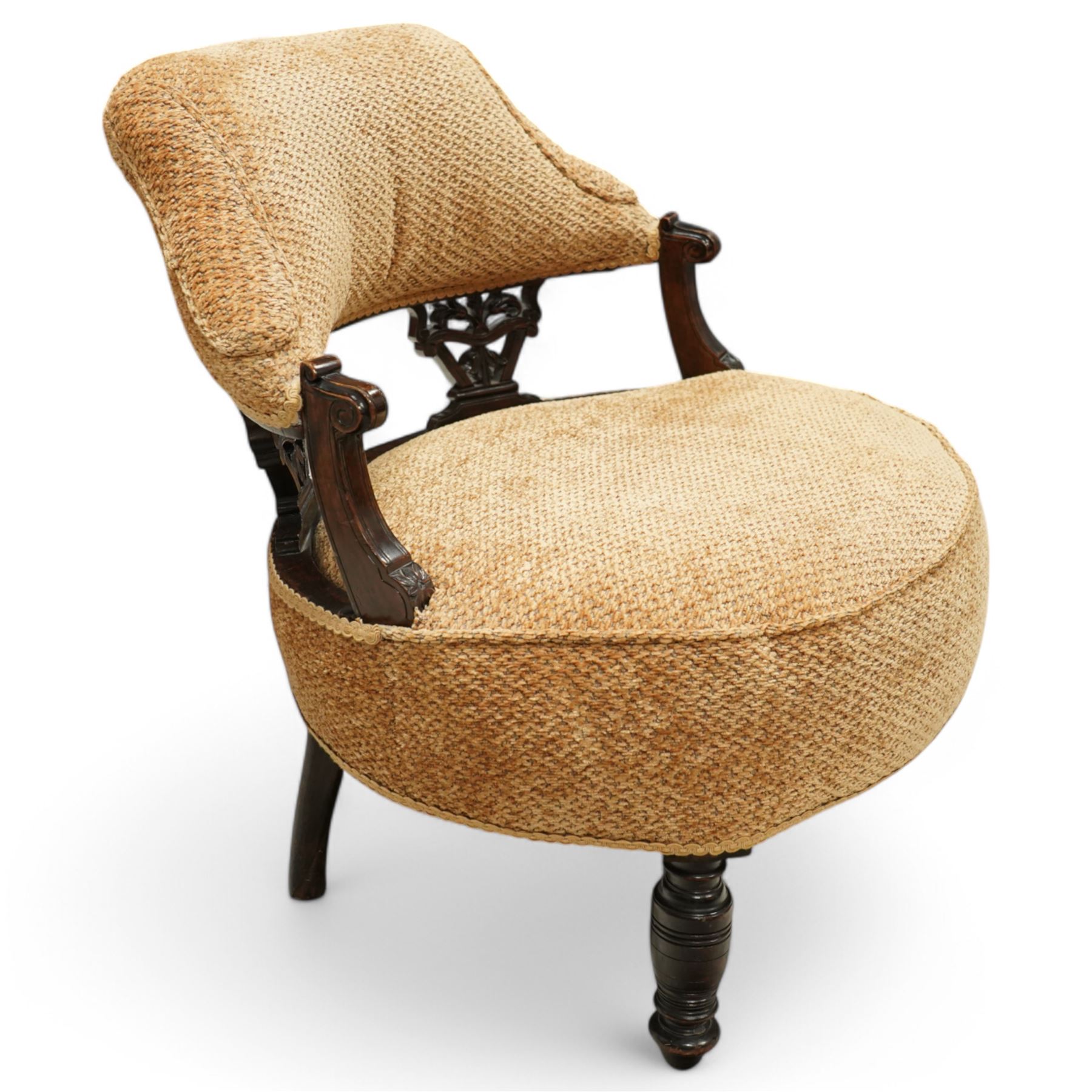 Late Victorian mahogany framed tub shaped chair, curved padded back and overstuffed seat in textured ochre fabric, pierced mahogany back supports with foliate and scroll carving, on turned front legs