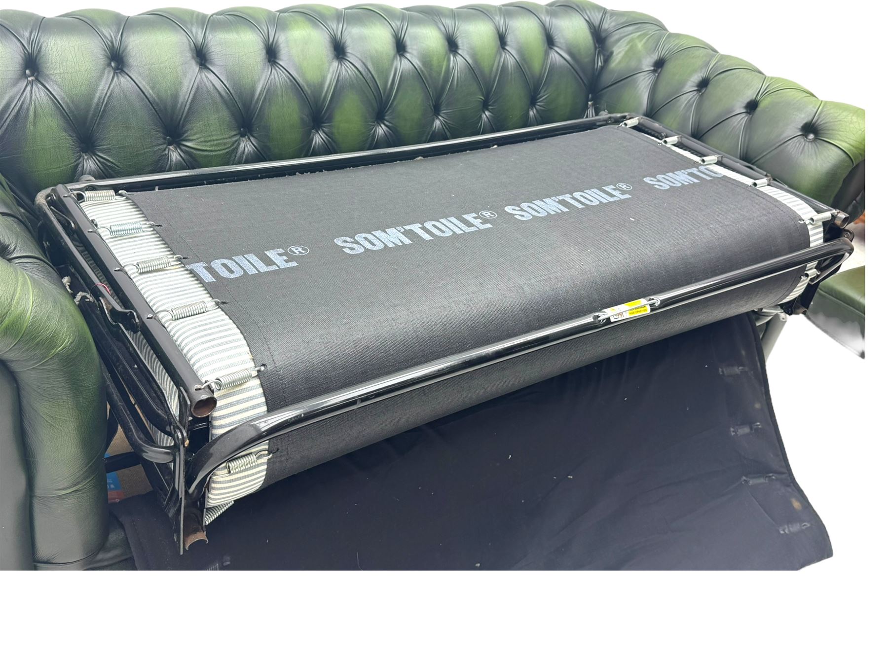 Two seat Chesterfield design sofa bed, upholstered in emerald green leather with deep-buttoned detailing, rolled arms, two loose seat cushions, and pull-out 