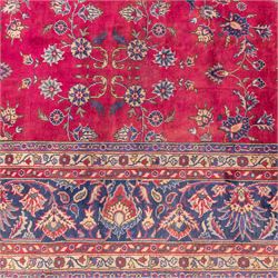 Large Persian-style mahal-type hand-knotted carpet, of rectangular form with a deep crimson field decorated with an all-over arrangement of stylized floral sprays and palmettes, with a central subtle medallion composition enclosed by a dark navy main border of scrolling floral motifs between narrow guard stripes with fringe ends 