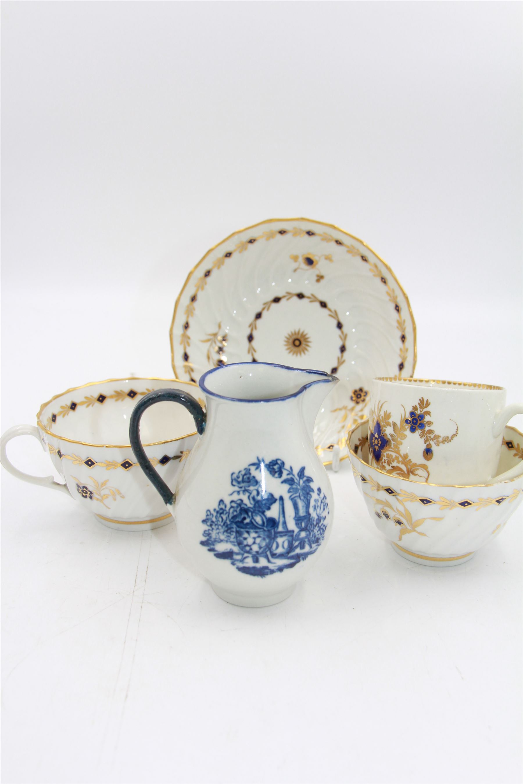 18th century Caughley blue and white sparrow jug, decorated in the Mother and Child pattern, circa 1780-1790, with underglaze C mark beneath, H9cm, together with a Worcester coffee cup, circa 1785 painted with floral sprays in underglaze blue and gilt, with crescent mark beneath, and a Caughley trio of tea cup, tea bowl and saucer, each of moulded wrythen fluted form and decorated with gilt and blue sprigs and bands, each with crescent mark beneath, (5)