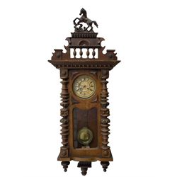 1890’s German striking wall clock in a walnut case, striking the hours and half hours on a coiled gong, eight-day Juhngans movement with a two-part dial, Roman numerals, gothic steel hands and visible gridiron pendulum, case with turned pilasters, applied carving and glazed full length door.

