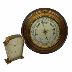 A mid-20th century  hall barometer with a compensated Aneroid movement, sixteen-centimetre silver painted dial measuring barometric air pressure from twenty-six to thirty-one point nine inches, weather predictions and trend written in black upper- and lower-case gothic script and roman capitals with a blue steel indicating hand and brass recording hand, brass effect bezel with flat bevelled glass, dial inscribed “Made in England”

With a 1950’s Smiths eight-day timepiece mantle clock.
