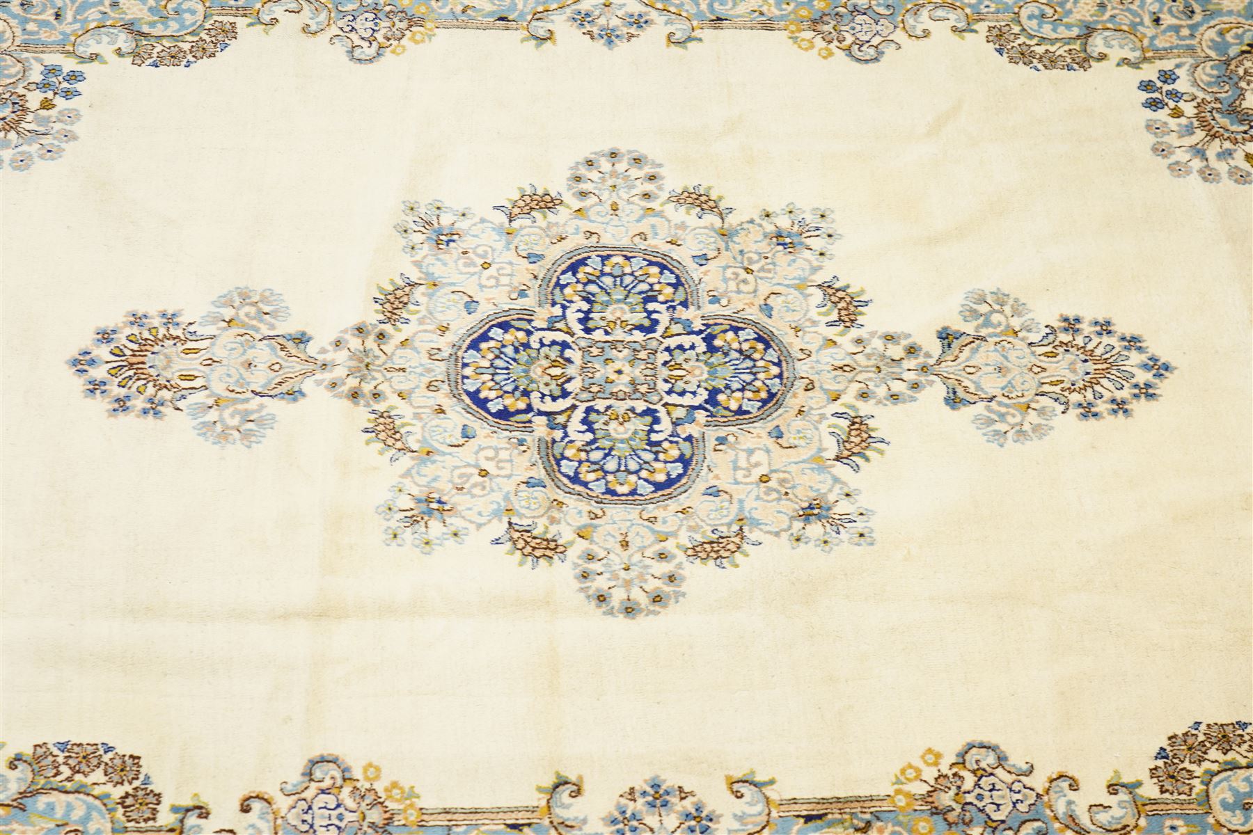 South East Persian Kirman hand-knotted carpet, ivory field with central floral medallion in tones of cobalt and pale blue, issuing scrolling vinery and palmettes, conforming spandrels, main border with scrolling foliage and stylized palmettes, framed by multiple guard borders, with cotton fringe ends 