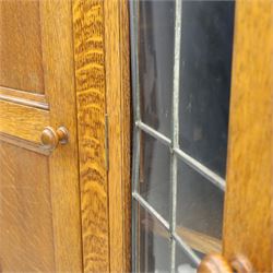 Edwardian oak glazed cabinet, moulded cornice above a panelled front and sides, fitted with lead glazed doors enclosing shelved interior, left side full length cupboard converted to enclose a gun cabinet, on a plain plinth base 