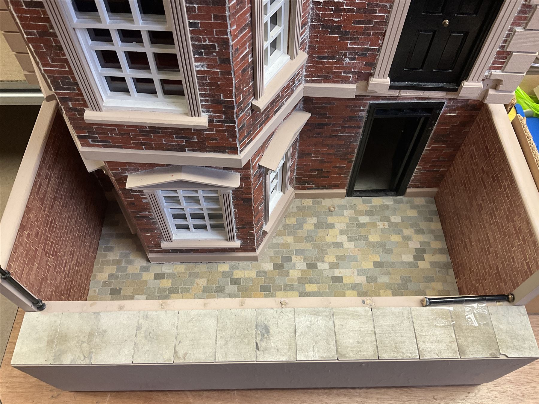 'The Hollies' - good quality sectional wooden doll's house in the form of a Georgian style four-storey bay windowed town house with simulated brick front elevation, rendered sides, off-set corner stonework, faux slate-hung top floor with flat roof and chimney stack, working sash windows, iron railings around front basement courtyard with hinged front elevation to two rooms with  spiral staircase, side hinged central section approached by external steps with iron balustrades to the sides leading to a front door, entrance hall with stairs to landing and two rooms on two floors with dado panelling and fire-surrounds, the top floor with top hung front elevation revealing stairs to a landing and bedroom; wired for electricity L51cm D65cm H107cm including chimney; together with a good quantity of quality wooden furniture and accessories including piano, dressers, bookcase and books, rugs, double half-tester bed, metalware, pictures etc