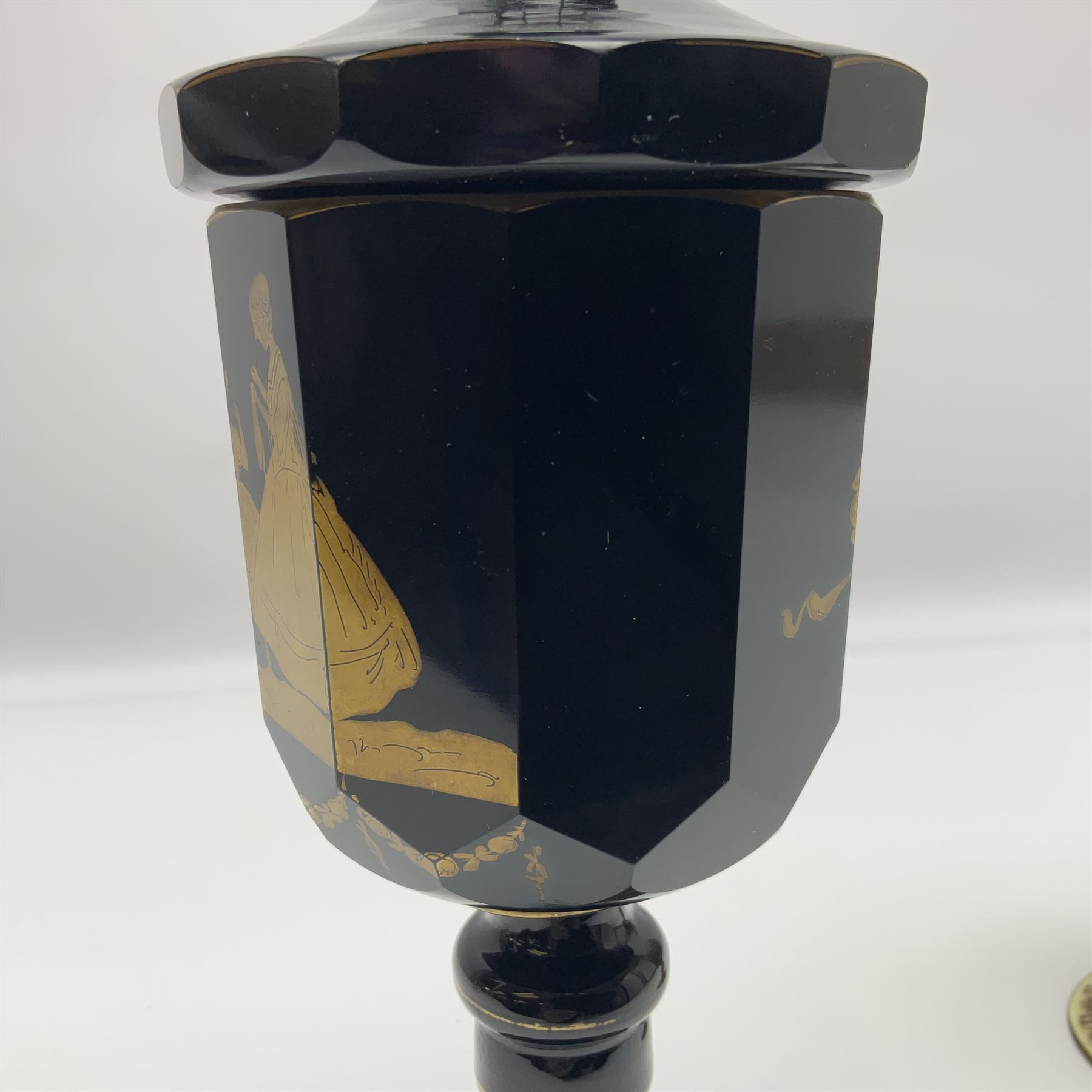 19th Century Bohemian amethyst glass lidded goblet, the bowl of faceted form, gilded with three children in period dress playing games, upon a knopped stem and conforming faceted foot, together with an art nouveau green glass goblet, with gilded rim, upon clear trumpet stem, and a hand blown wine glass, transfer printed with birds and three figures in period dress, tallest H29cm