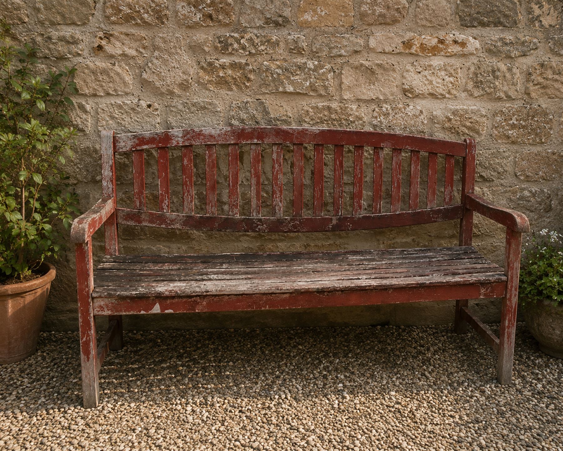 Teak garden bench, with slatted seat and spindle back, shaped armrests, finished in weathered red painted finish.
