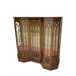 Early 20th century mahogany Gothic style display cabinet, faceted reverse break front, enclosed by three doors with pointed arch astragal glazing, on stepped and moulded plinth base