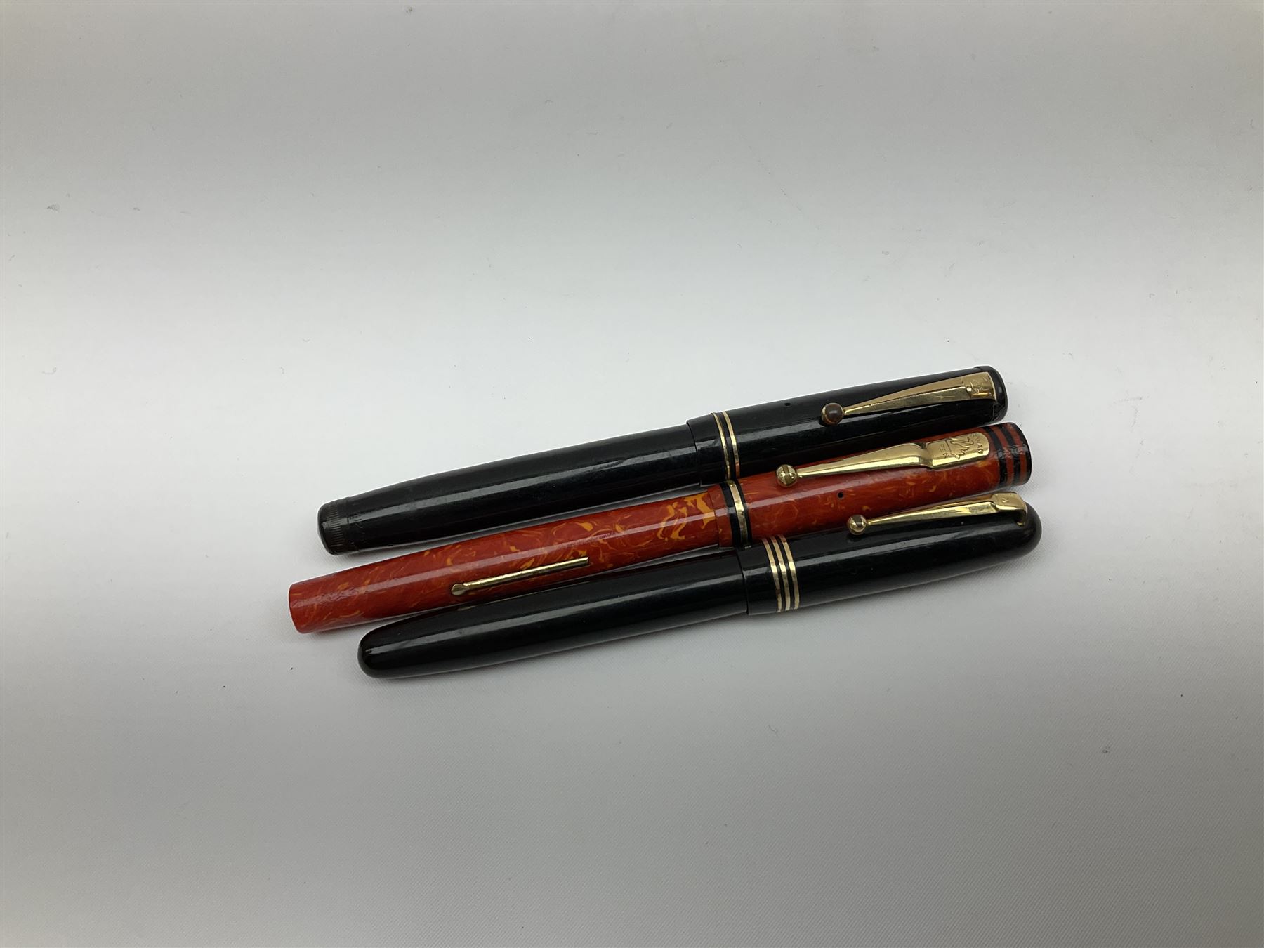 Vintage Swan Mabie Todd lever fill fountain pen in coral red, the nib a/f marked 14K, together with two further vintage Swan Mabie Todd fountain pens, the first example with lever fill, the other leverless, each with black body, one with nib marked 14ct, (3) 