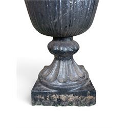 Pair of Victorian large scale cast iron garden urns, flared petal shaped rim with tapering waist, gadrooned base on square plinth, finished in black paint