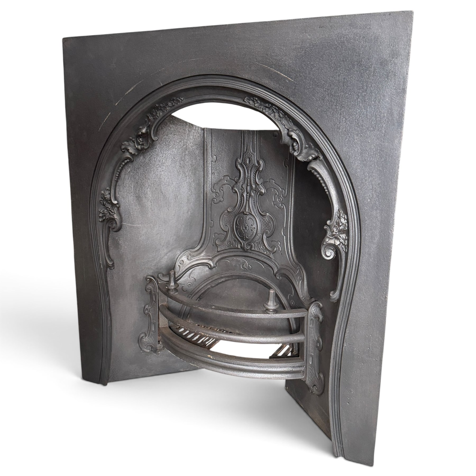 Victorian cast iron fireplace, the arched surround cast with scrolling foliate ornament and central shield-shaped cartouche, fitted with a bowed fire basket, in black painted finish