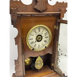 An early 20th century spring driven alarm clock in the style of an American  “gingerbread” shelf clock, rectangular wooden case with applied incised mouldings on a shaped taper foot plinth, full length glazed door with flowers and leaves, visible gilt pendulum bob, with a painted white metal dial inscribed “Fattorini & Sons Patent Automatic Alarm”, roman numerals and minute track with brass alarm setting disc, steel spade hands, spun brass bezel with winding apertures, alarm sounding on both a coiled gong and bell, two advertising/trade labels pasted to the case backboard.
