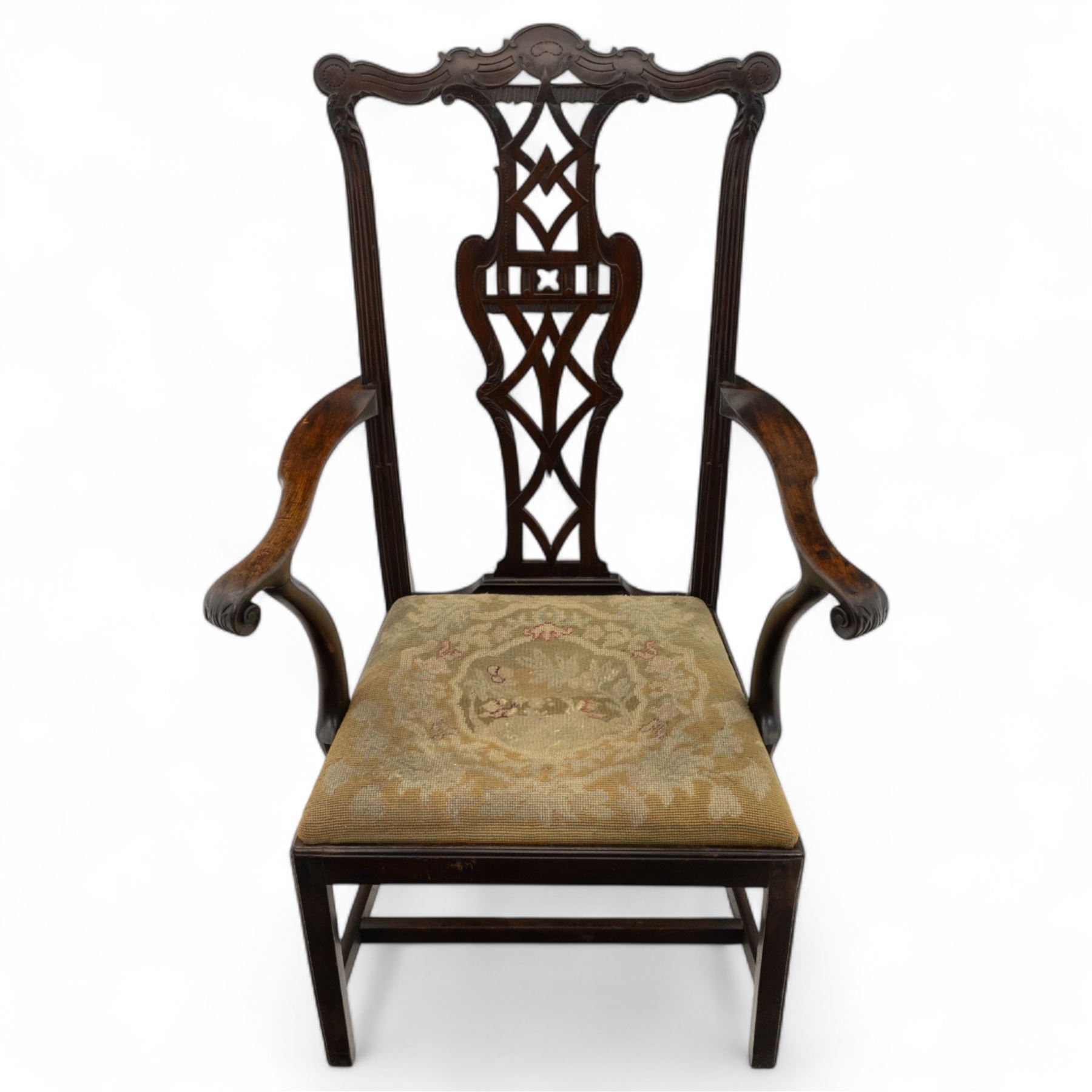 19th-century Chippendale Revival design mahogany oversized high-back armchair, serpentine crest carved top rail above pierced back splat with interlaced ribbon carving and geometric fretwork design, and outward scrolling arms above drop-in needlework seat on square chamfered legs 