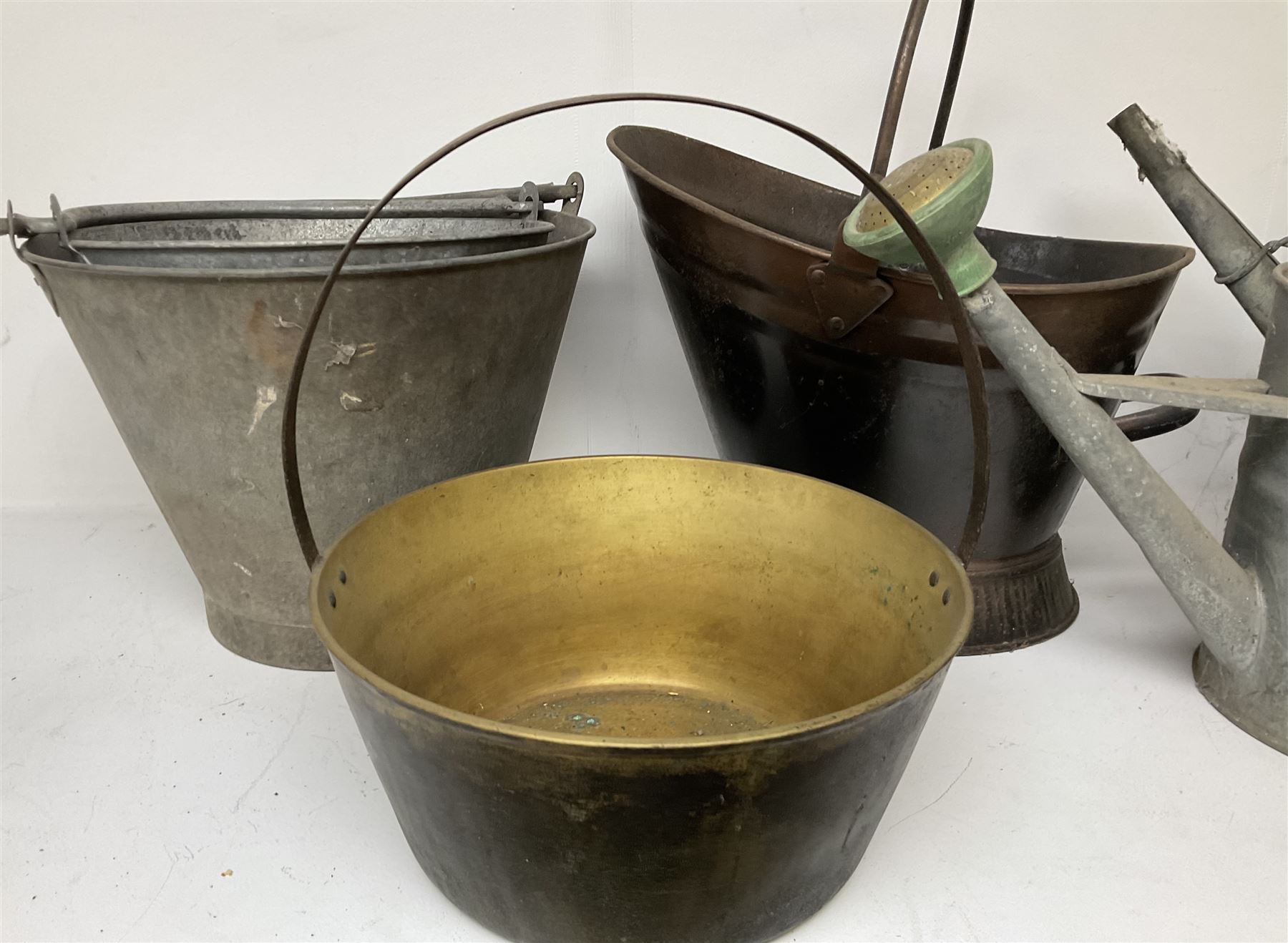 Two vintage galvanised watering cans, three galvanised buckets and a brass jam pan