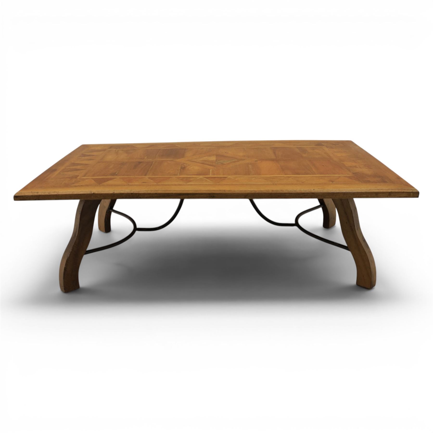 20th century Spanish design oak coffee table, rectangular parquetry top with geometric star and triangular inlaid decoration, moulded edge, on shaped trestle end supports united by black painted wrought iron scroll stretchers